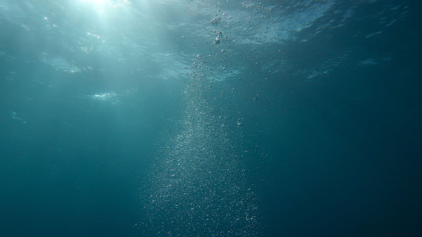 Aufsteigende Blasen im Wasser, durchflutet von Licht von der Oberfläche